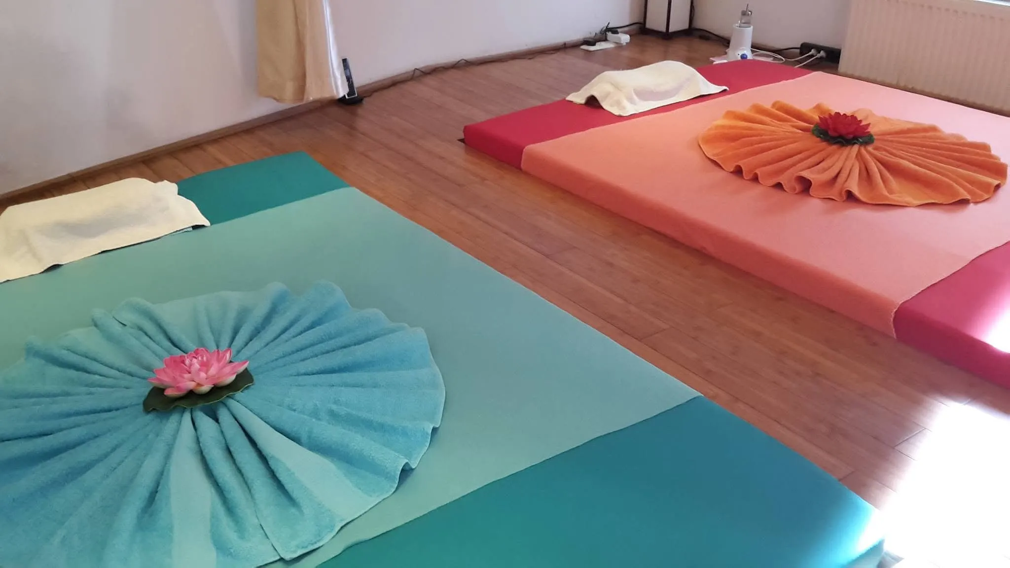 Zwei Massagematten mit gefalteten Handtüchern und einer Lotusblüte im Behandlungsraum